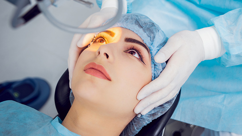 female eye doctor patient lying down undergoing lasik procedure, yellow light shining in eye